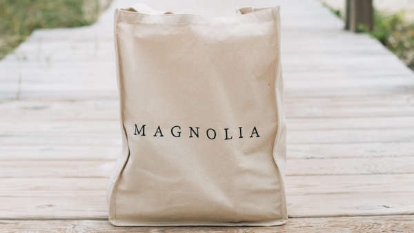 A beige, rectangular branded tote bag with the words ‘MAGNOLIA’ printed on the front.